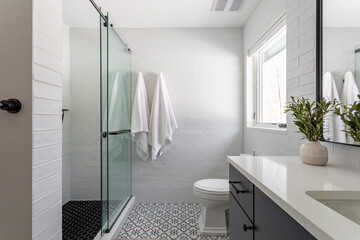 Bright modern bathroom with glass walk-in shower, white subway tile walls, patterned floor and...