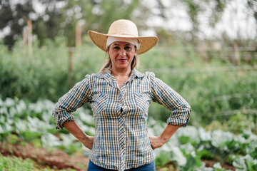 Portrait of a confident mature female farmer standing in her vegetable garden wearing a straw hat and plaid shirt.