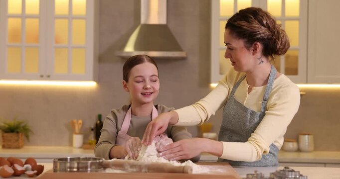 Smiling mother and her daughter cooking together at table in kitchen
