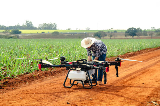 Modern farmer preparing a large agricultural spraying drone on a dirt road next to a green crop field for precision farming