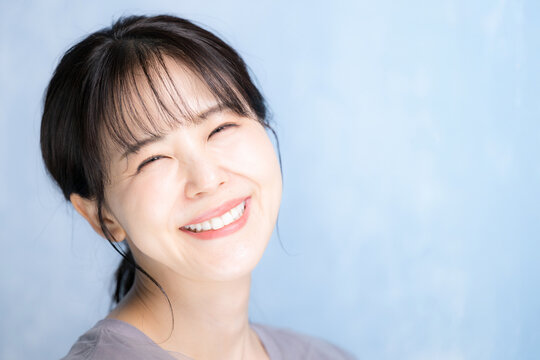 水色背景で美容やスキンケアの明るいイメージのクローズアップ　笑顔で考えるカメラ目線　大笑いの幸せのイメージ