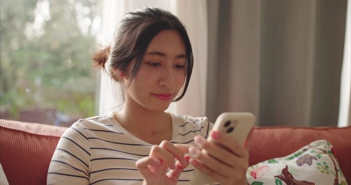 Smiling Young Asian Woman Using Smartphone on Sofa - Online Shopping and Social Media Lifestyle Concept