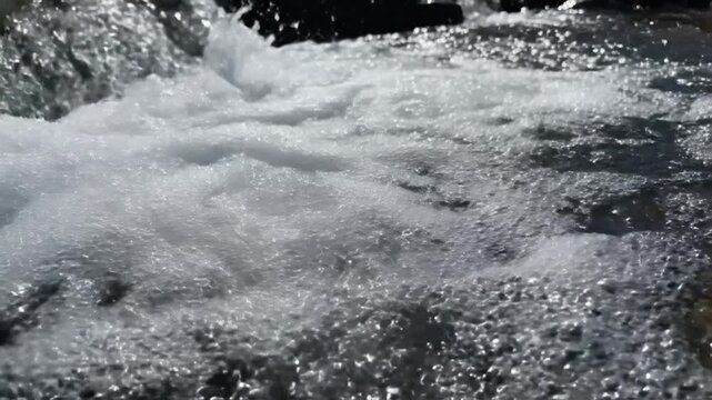 Close-up of turbulent water flowing over rocks, white foam and bubbles