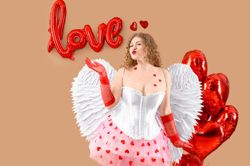 Fototapeta premium Sexy young woman dressed as Cupid with balloons blowing kiss on beige background. Valentine's Day celebration