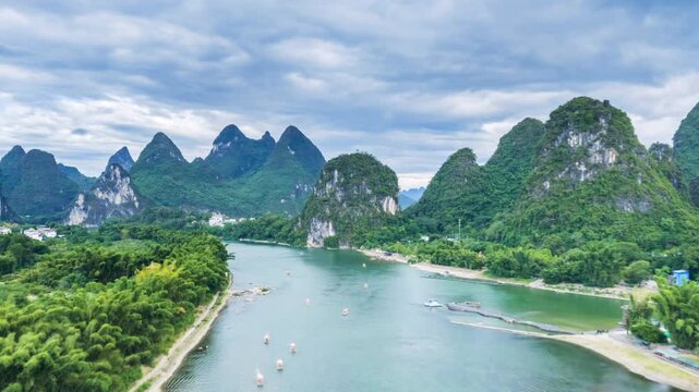 Aerial time-lapse of Li River near Yangshuo Bridge, karst peaks, emerald waters, and bamboo rafts under cloudy sky in Guilin&rsquo;s iconic landscape.