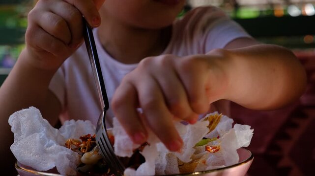 Child girl eating spicy salad with seafood, fuzhou, squid, mix vegetables, peanut, sesame, mushroom, crispy puffed rice. Vacations and having lunch in the terrace of guest house hotel.
