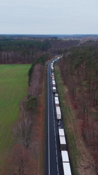 Vertical Screen Aerial View Packed Truck Queue On Narrow Highway, Tight Single Lane Flanked By Trees, Slow Moving Freight Convoy, Delivery Trailers Backed Up Through Countryside, Poland