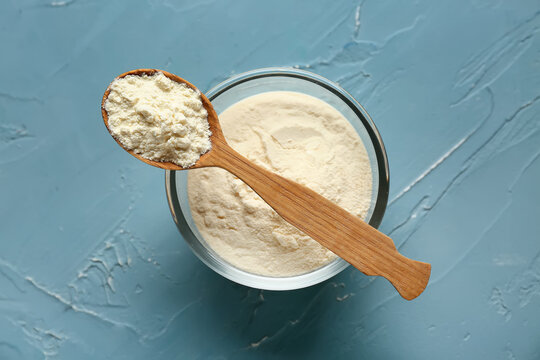 Bowl of powdered milk and wooden spoon on blue grunge background