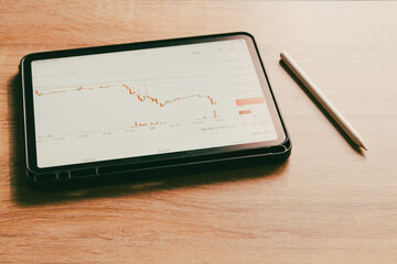 Digital tablet displaying financial trading chart on wooden table, professional workspace for stock market analysis and investment.