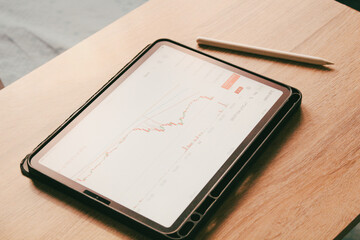 Digital tablet displaying financial trading chart on wooden table, professional workspace for stock market analysis and investment.