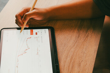 Close up of hand using stylus pen pointing at stock market candlestick chart on tablet, concept of technical analysis and trading signal.