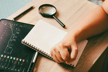 Successful businessman clenched fist on notebook with financial stock market tablet, concept of achievement and trading determination.