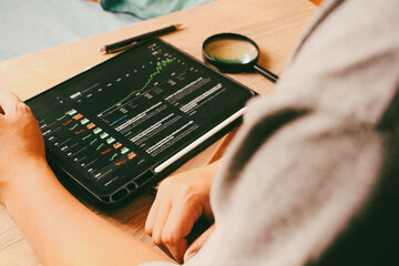 Investor watching stock market trading charts on digital tablet at wooden desk, concept of financial analysis and home office workspace.
