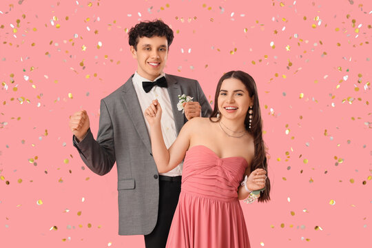 Happy prom couple with confetti dancing on pink background