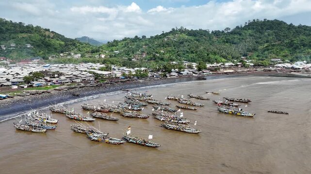 aerial perspective showing dozens of traditional fisherman wooden pirogues anchored along the dark volcanic sand beaches of Limbe