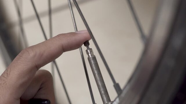 Close up hand pressing bike tire valve to release air, creating a sharp hissing sound that slowly fades as pressure drops.