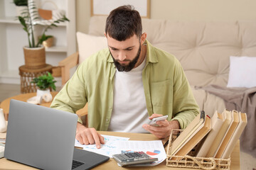 Obraz premium Young bearded man working with diagrams and laptop on table at home