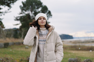 Obraz premium Winter woman outdoor fashion coat portrait in chilly countryside with sweater and beanie, soft light, calm landscape, cozy look for cold weather lifestyle.