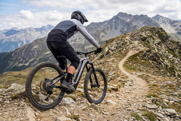 Fototapeta premium Electric mountain biker exiting technical alpine ridgeline trail