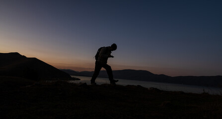 Obraz premium Silhouette of a hiker walking on a hill at dusk with a calm evening sky.