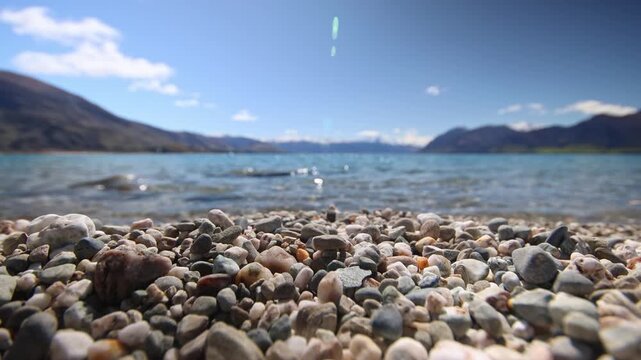 Static close focus wide angle shot of waves crashing on a pebble beach of Lake Hawea. Senic snowcapped mountrain in background.