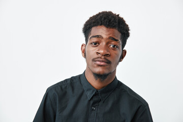 Obraz premium Young african man with dark skin and short curly hair wearing black shirt looking at camera with neutral expression on white background.