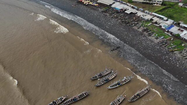 A detailed top-down aerial perspective showing dozens of colorful traditional fishing pirogues neatly arranged on the volcanic black sand of Limbe, Cameroon