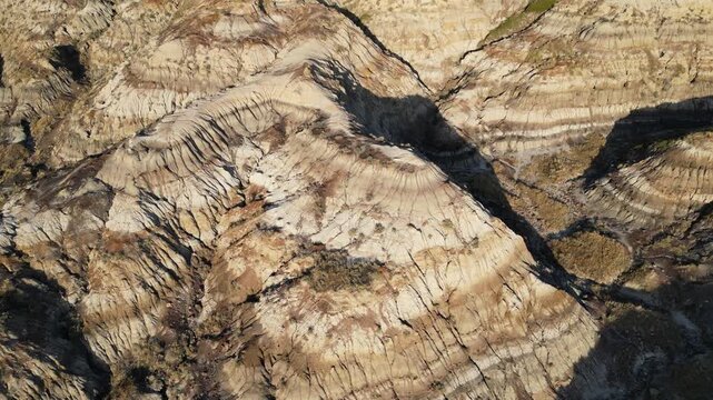 Aerial shot close to the ground toward eroded badlands hills in Alberta, Canada, with a steeper downward camera angle and strong side lighting creating high contrast near sunset.