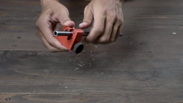 A close-up of a hand turning a pipe cutter on a metal alloy tent frame, producing a sharp metal grinding sound and a crisp snapping sound