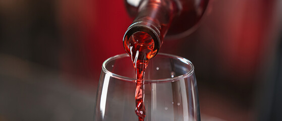 Pouring of red wine into glass on blurred background, closeup