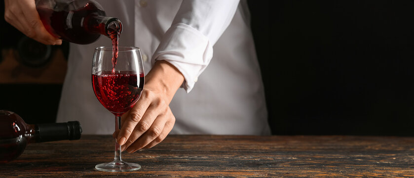 Female bartender pouring red wine from bottle into glass, closeup