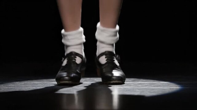 A dancer's feet, clad in shoes and socks, perform on a stage lit from below