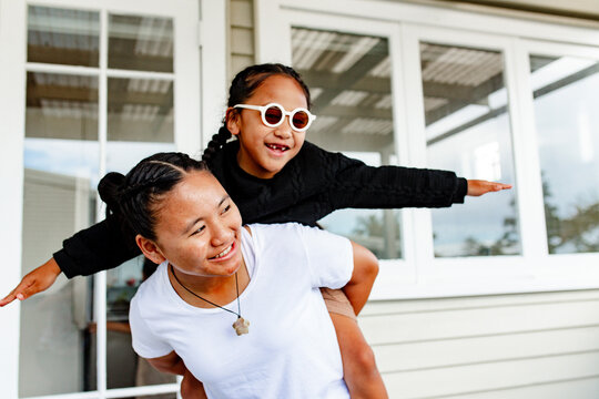 Teenage sister carrying younger brother on piggyback extending both arms like flying
