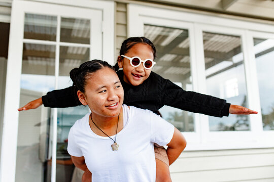 Teenage sister carrying younger brother on piggyback extending both arms like flying