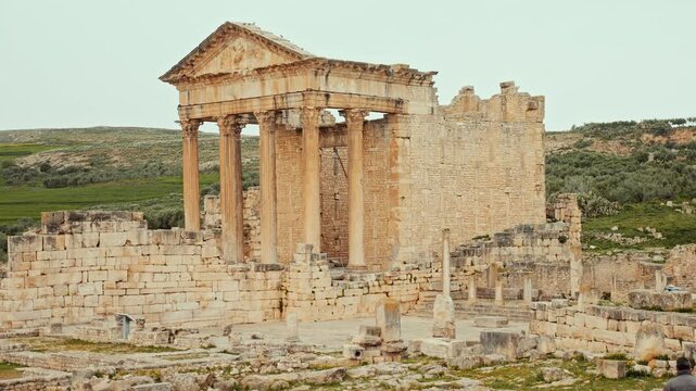 Well-preserved remnants of Capitol, historic temple with towering columns among ruins of ancient Roman settlement of Dougga in northern Tunisia on cloudy spring day