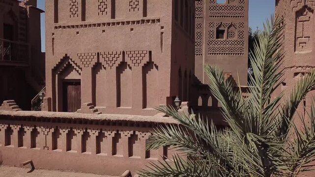 Medium shot showcasing detailed geometric clay ornamentation on a traditional Kasbah wall. The Berber design and crenellated architecture highlight Moroccan craftsmanship in Ouarzazate.