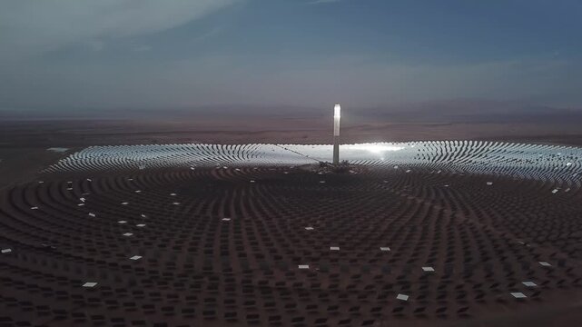 Aerial wide shot of the Noor Ouarzazate solar complex, specifically the Noor III central tower surrounded by thousands of mirrors (heliostats). It is the world's largest concentrated solar power (CSP)
