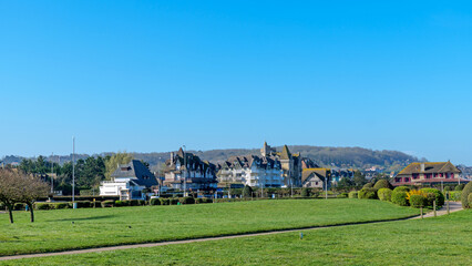 Fototapeta premium Urban park landscape in Deauville France with wide green field and walking path, traditional French seaside architecture in distance, soft natural light and peaceful spring mood