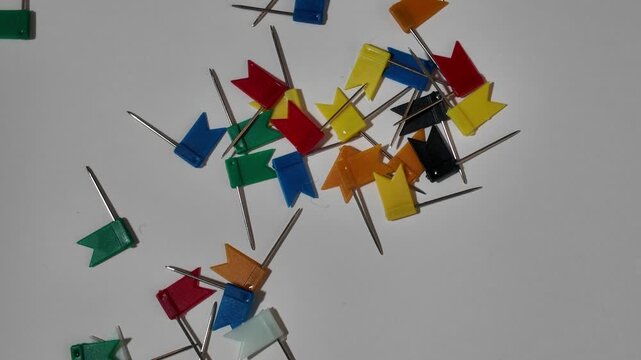 Multicolored plastic flag push pins fall on random locations Scattered on a White Background