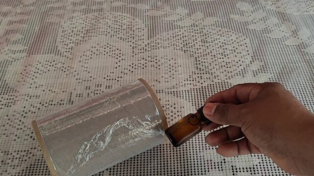Applying plastic wrap to a bottle of pine essential oil for secure delivery.