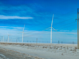 Windmills in snow field, clear blue sky background. Renewable energy generating power in a winter landscape with electric lines.