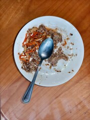 Leftover buckwheat dish with carrot and meat on a white plate with a spoon. Meal remains, food waste concept.