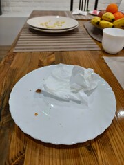 Dirty white plate with crumpled paper napkin on wooden table after meal. Concept of cleaning up dinner and food waste.