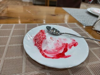 Leftovers of an unhealthy cake on a white plate with a spoon. Concept for food waste or after party mess for cleaning.