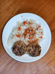 Two meatballs with rice and carrots on a white plate. Homemade cooked meal with meat and grain. Healthy lunch or dinner concept.