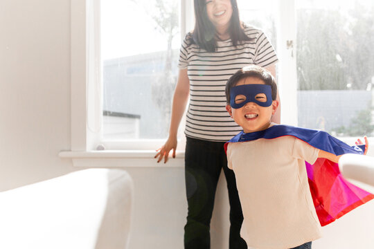 Asian boy wearing superhero costume in the bedroom with mum standing beside him