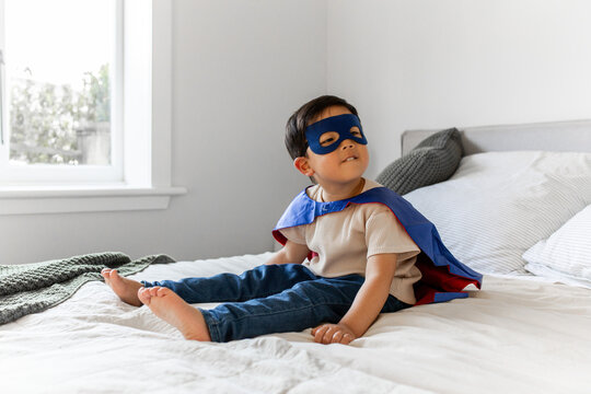 Young Asian boy in superhero costume sitting on the bed