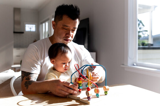 Asian father playing colourful bead maze toy with toddler daughter on the table