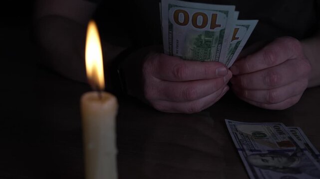 Under the soft, dancing light of a solitary candle, hands meticulously sort and stack crisp United States 100 dollar notes.