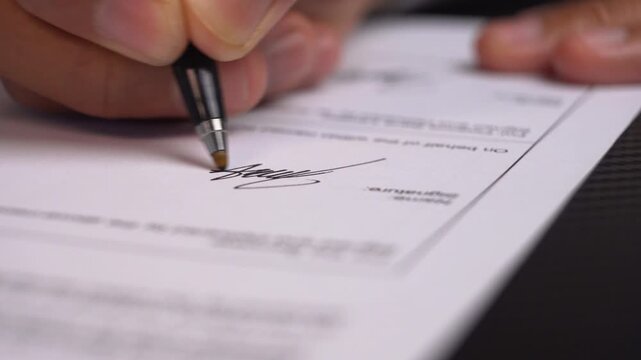 Person's hand writing signature on business deal contract document for approval process